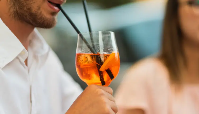 Un uomo sorseggia un Aperol Spritz, perfetto per la sua aperitivo ricetta. Ghiaccio e arancia completano il drink.