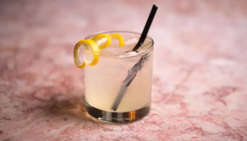 Un rinfrescante Vodka Sour IBA, guarnito con scorza di limone, su un tavolo di marmo rosa.