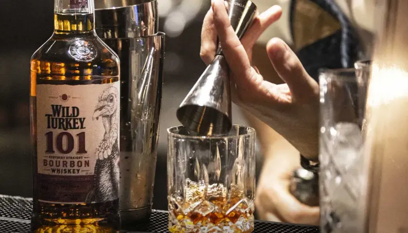 Un barista prepara un bourbon drink versando il Wild Turkey 101 in un bicchiere con ghiaccio.