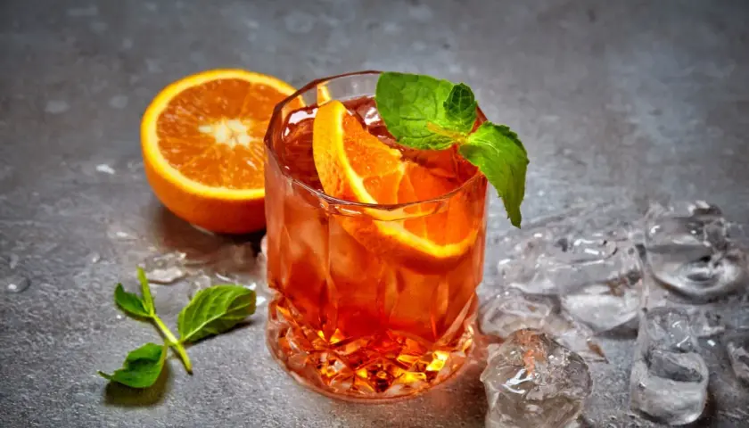 Rinfrescante cocktail con ghiaccio tritato, arancia e menta. Perfetto per un aperitivo estivo.