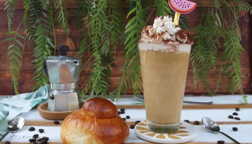 Un bicchiere di caffè freddo siciliano con panna e cacao, accanto a una brioche e una moka.