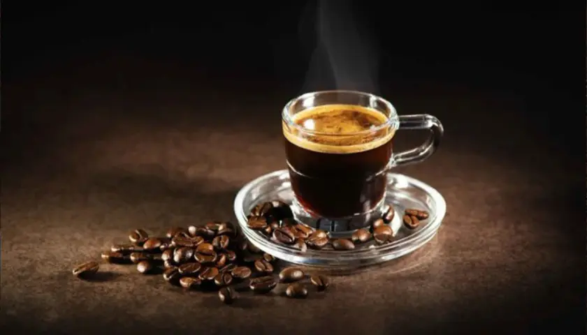 Un fumante caffè al vetro, con chicchi tostati sparsi attorno, evoca un momento di puro piacere.