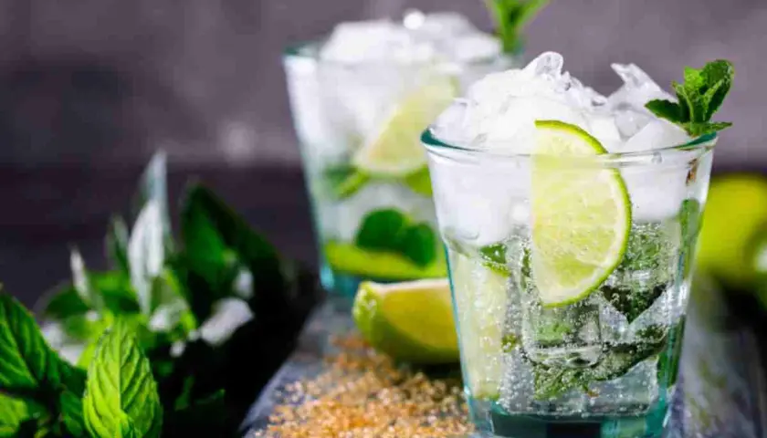 Due bicchieri di mojito, con menta fresca, lime e ghiaccio tritato. La ricetta perfetta per un'estate rinfrescante.