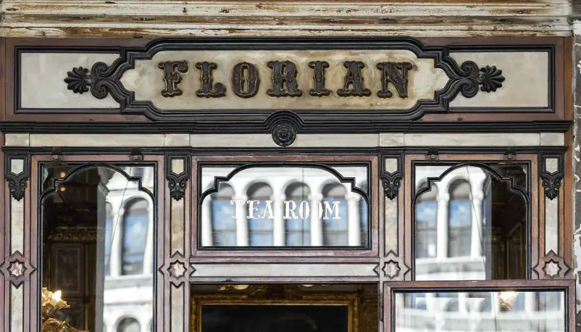Ingresso del storico **Cafe Florian**, con insegna in rilievo e riflessi di palazzi veneziani nelle vetrate.