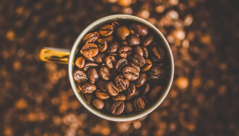 Tazza piena di chicchi di caffè tostati, un invito a gustare la bevanda che fa passare la fame.