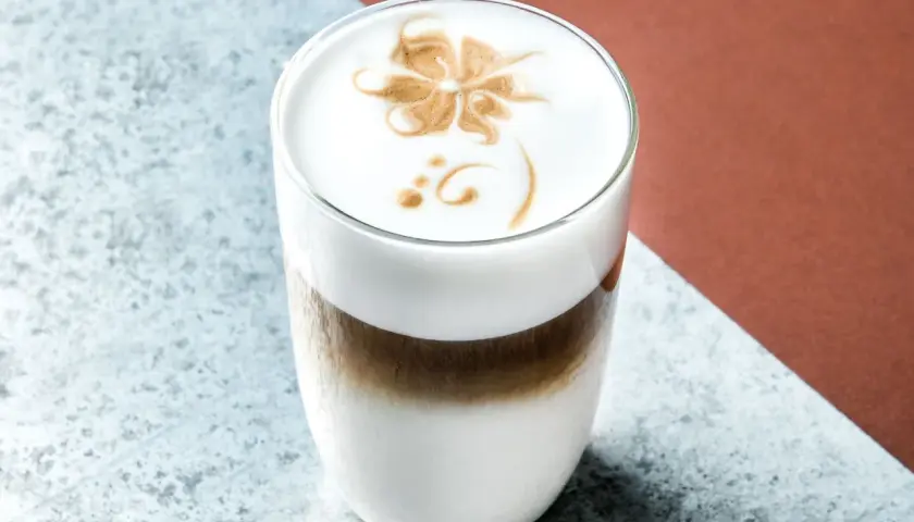Un delizioso cappuccino freddo con schiuma decorata a forma di fiore, servito in un bicchiere trasparente.