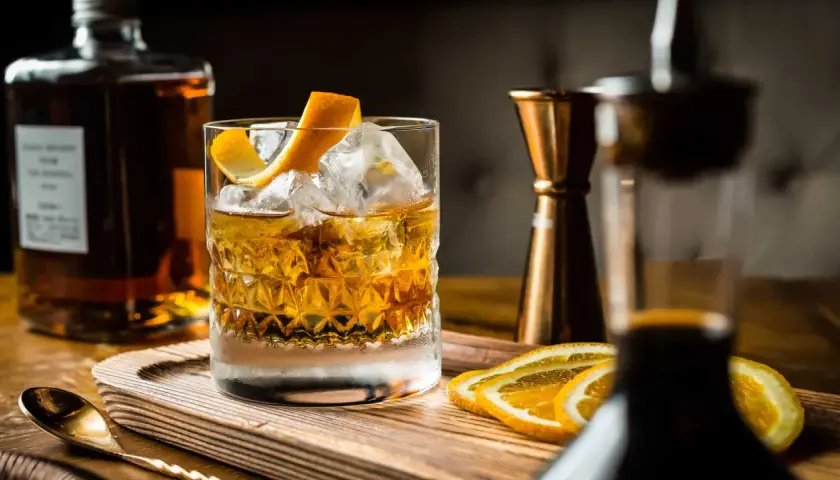 Cocktail con ghiaccio, scorza d'arancia e fette d'arancia. Ingredienti per un drink giapponese, con bottiglia di whisky e jigger in rame.