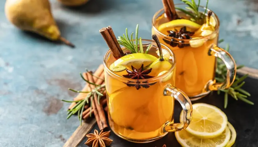 Due bicchieri di grog bevanda calda, guarniti con cannella, anice stellato, limone e rosmarino.