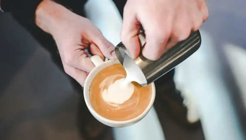 Mani esperte versano latte per cappuccino, creando un disegno sulla schiuma.