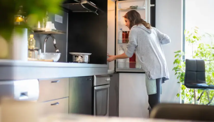 Donna prende una bottiglia dal frigo. Forse cerca il caffè in frigo per preparare una bevanda rinfrescante.