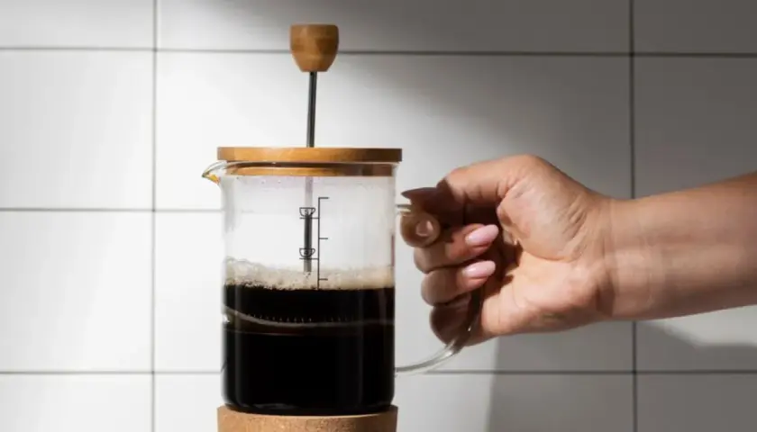 Mano che tiene una french press con caffè scuro. La scelta del quale caffè per french press è fondamentale per un aroma intenso.