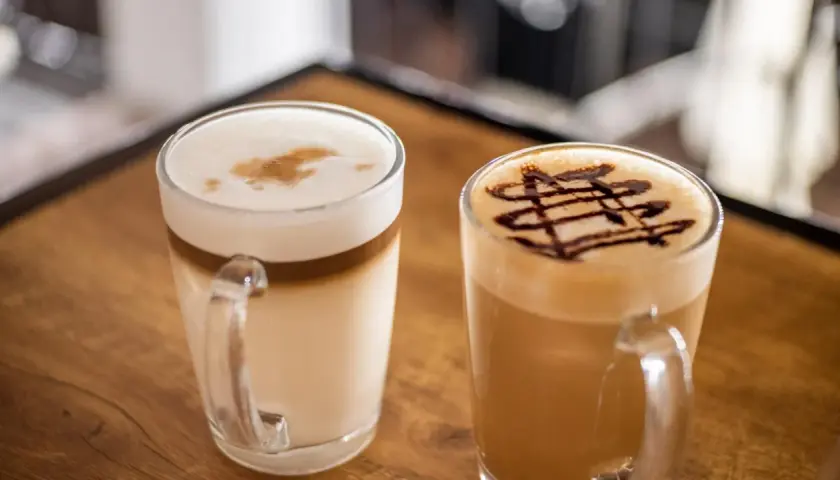 Due caffè in tazza: un macchiato vs latte con schiuma e decorazione al cioccolato.