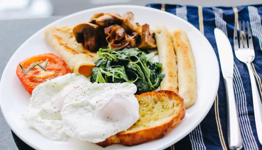 Un piatto ricco per una colazione continentale: uova in camicia, pomodoro, funghi, spinaci, pane tostato e salsicce.