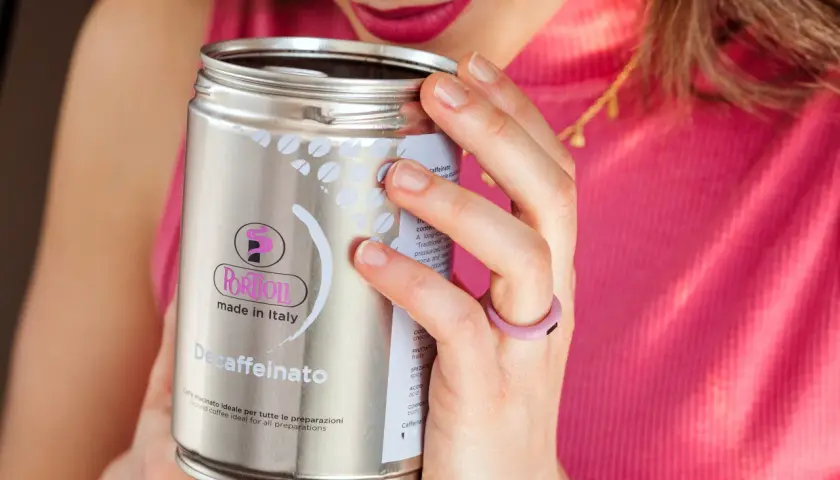 Donna annusa una lattina di caffè decaffeinato, godendosi l'aroma. Un caffè con meno caffeina, perfetto per ogni momento.
