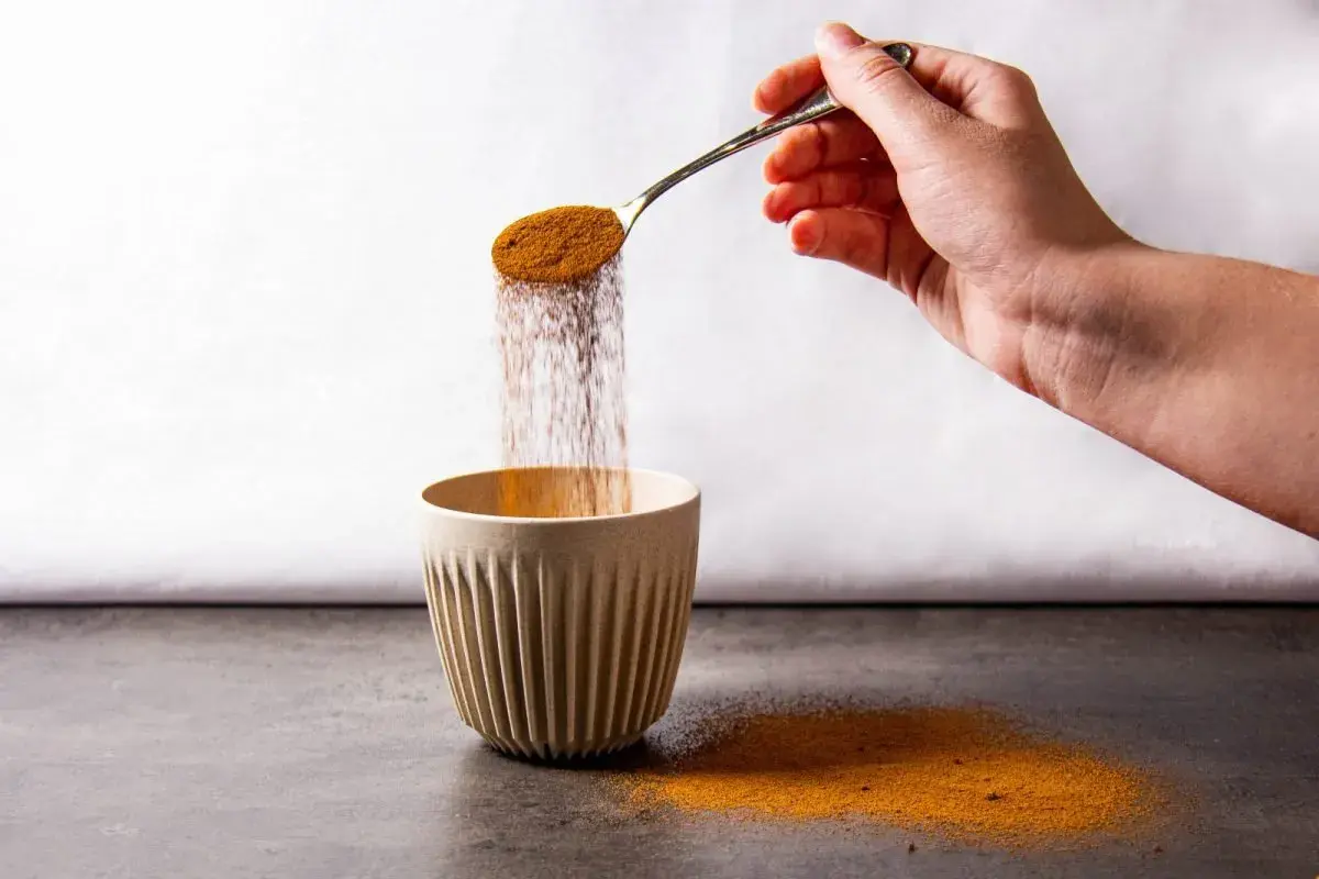 Mano versa polvere da un cucchiaio in una tazza. Forse è caffè solubile, ma fa male.
