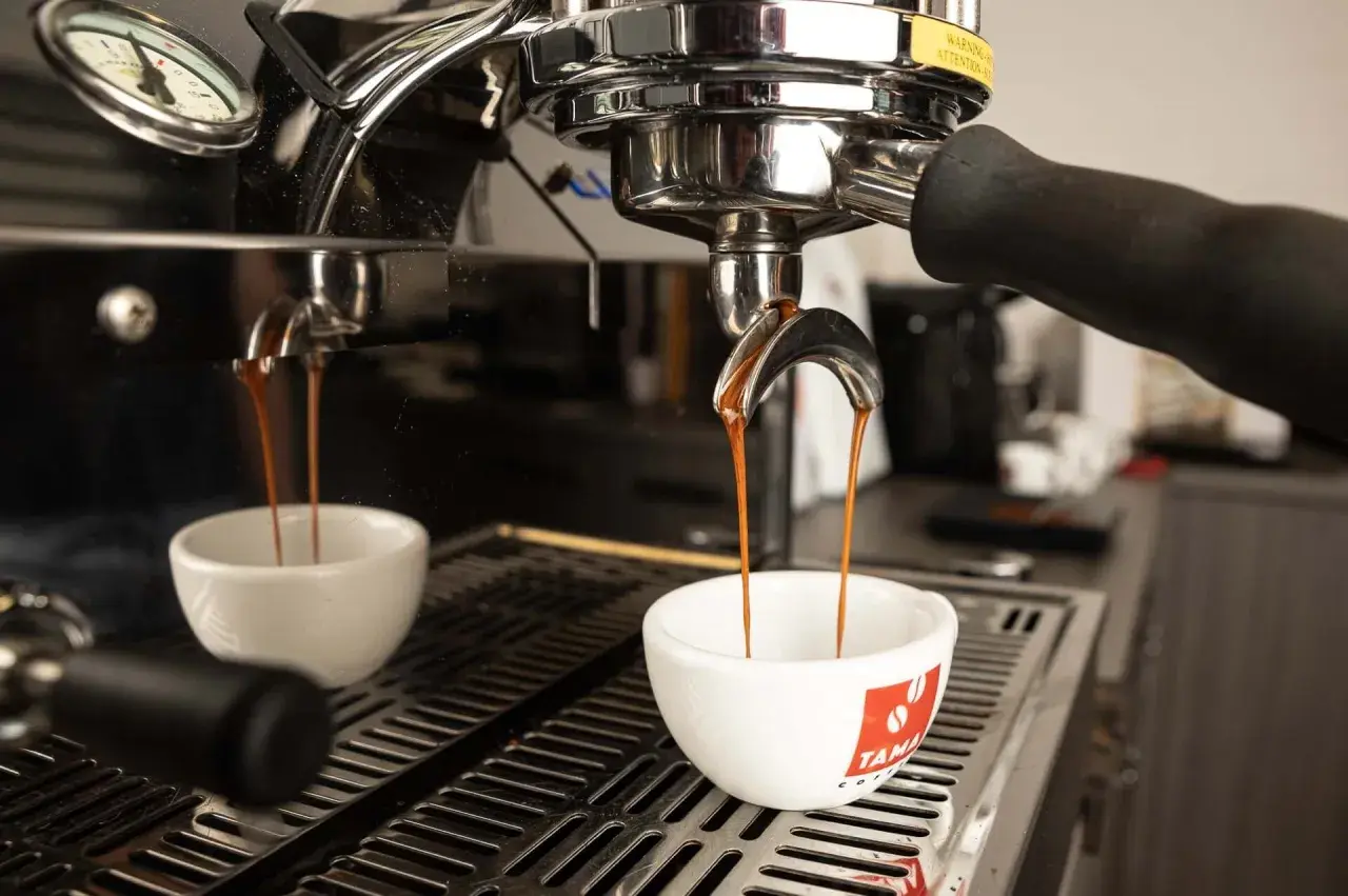 Due tazze bianche ricevono il prezioso liquido scuro, il caffè espresso, dalla macchina professionale.