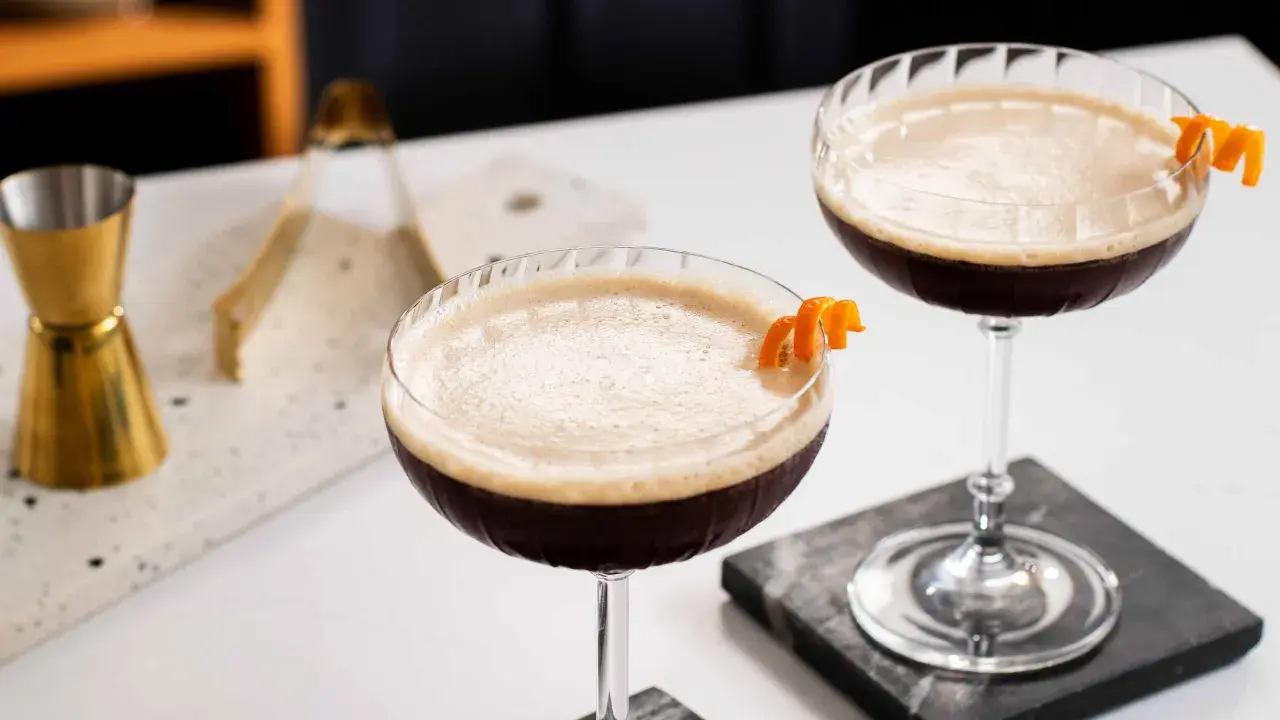 Due cocktail scuri con schiuma chiara, guarniti con scorza d'arancia. Un'idea per un caffè e succo d'arancia rivisitato.