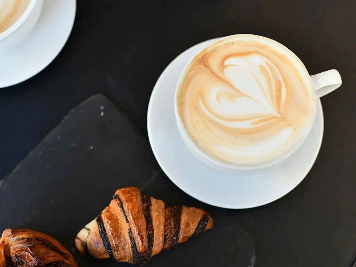 Un cappuccino con latte art a forma di cuore e croissant per una perfetta colazione al bar.