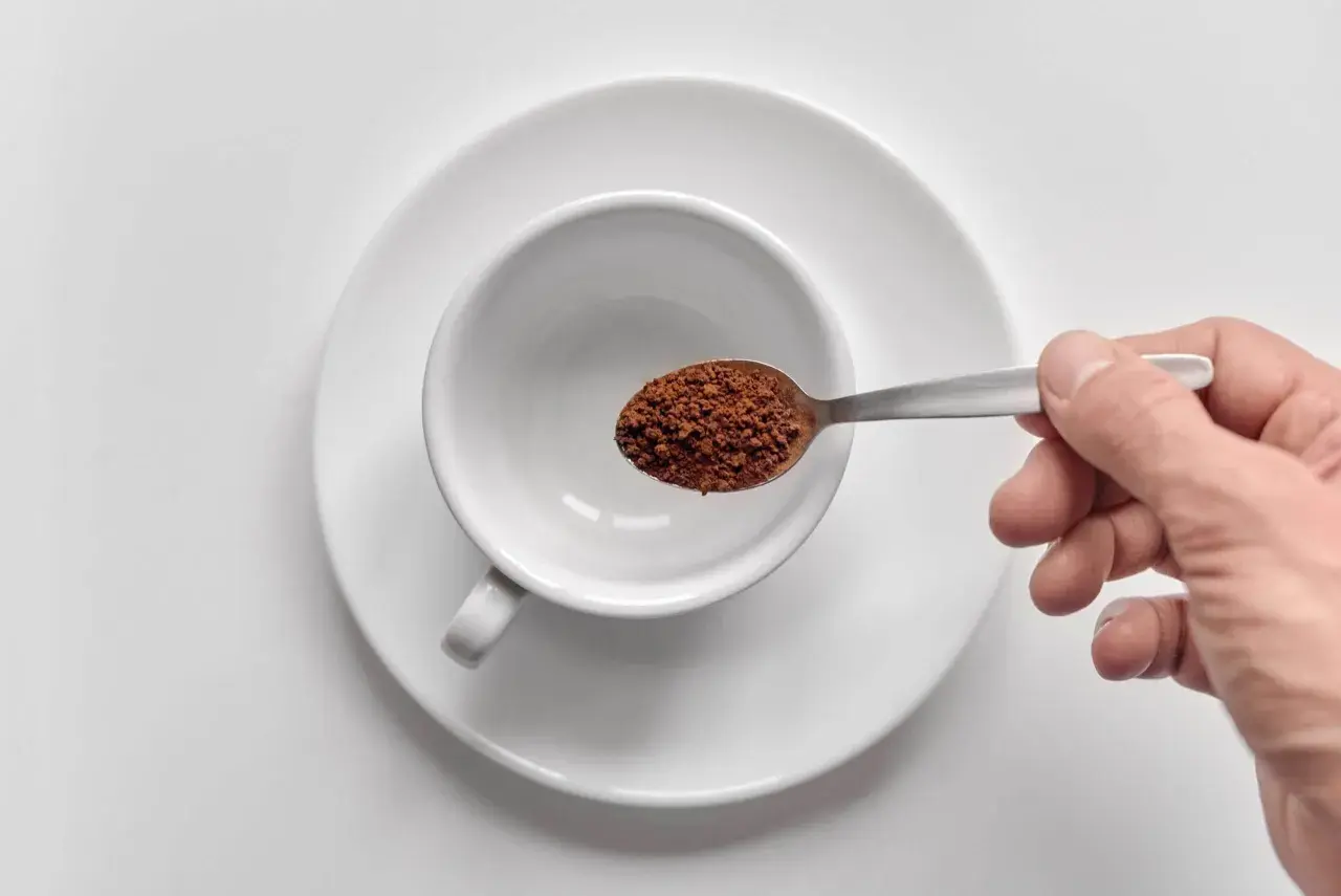 Mano che versa orzo café in una tazzina bianca.