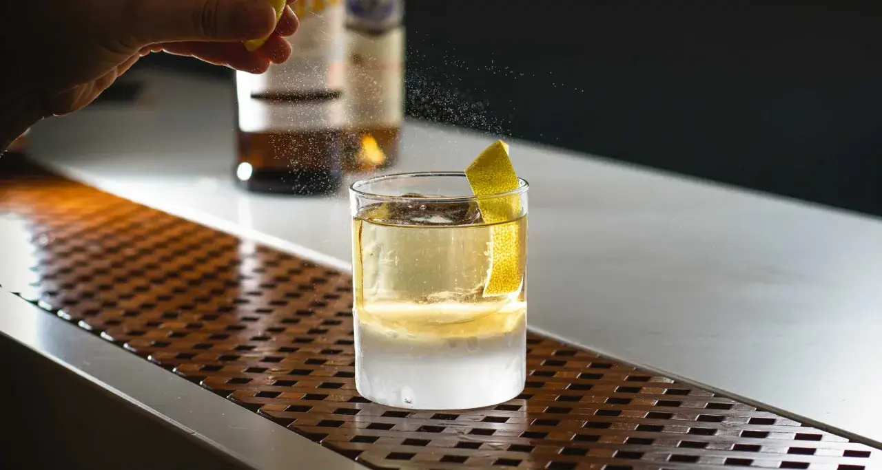 Un barista completa la negroni ricetta bar con una scorza di limone. Ghiaccio e liquore dorato in un bicchiere.