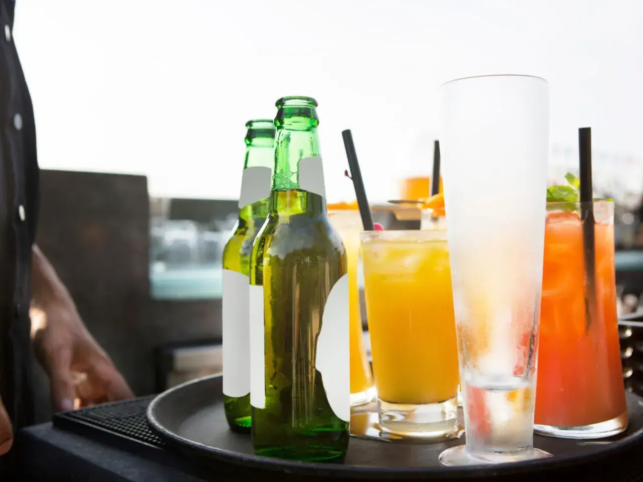Un cameriere serve un aperitivo originale: birre fresche e cocktail colorati su un vassoio.