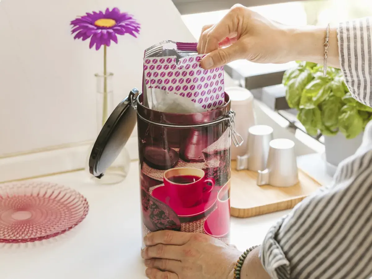 Mano inserisce pacchetto di caffè sottovuoto in un barattolo decorato. Freschezza garantita!