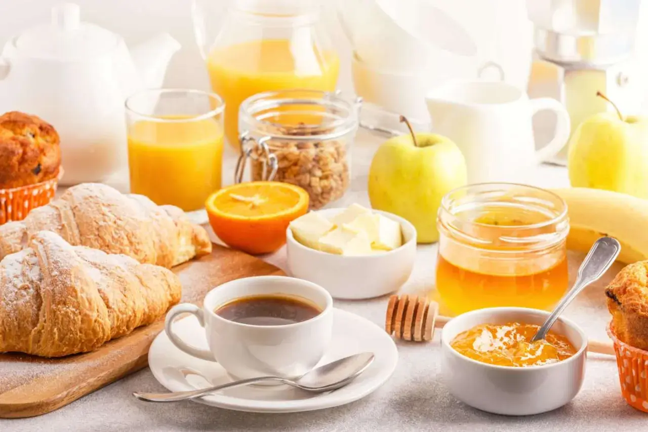 Un tavolo imbandito con croissant, caffè, succo d'arancia, frutta e marmellata, perfetto per delle bevande per colazione.