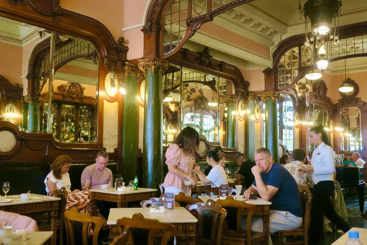Interno di un **majestic cafe porto** con arredi d'epoca, specchi e clienti seduti ai tavoli.
