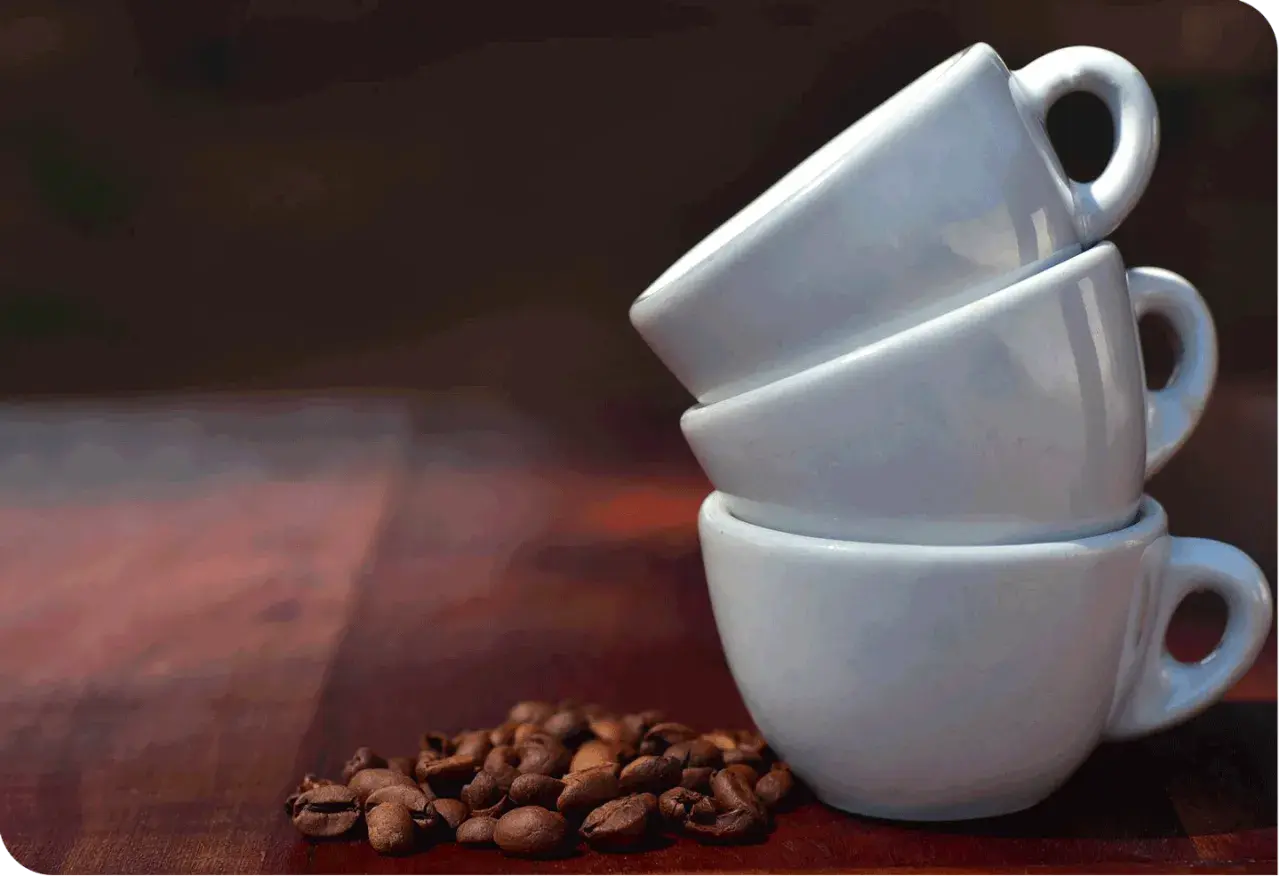 Tre tazzine bianche impilate, con chicchi di caffè tostati in primo piano. Immagina quanto contiene una tazzina di caffè.