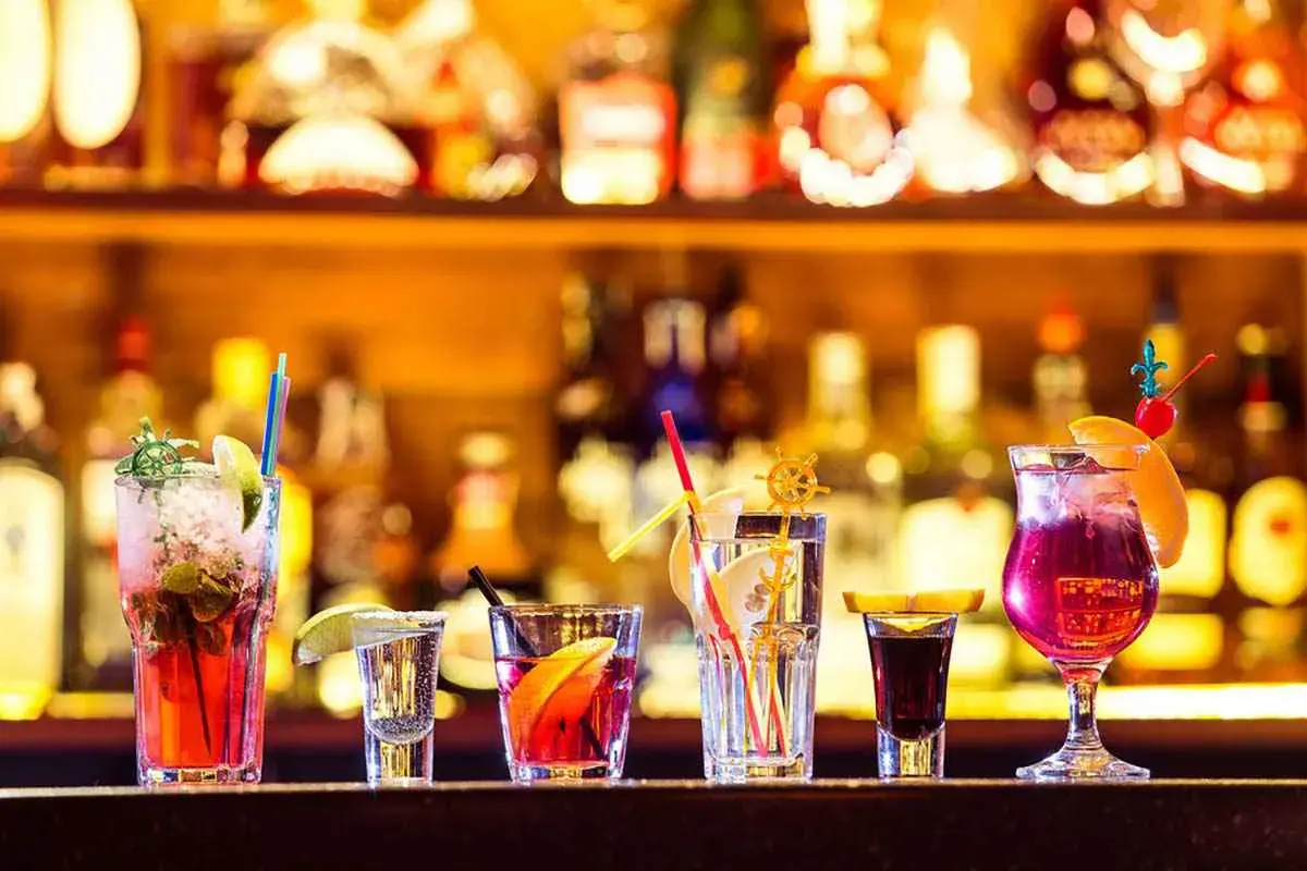 Varietà di cocktail principali colorati e rinfrescanti, guarniti con frutta e cannucce, su uno sfondo di bottiglie illuminate.