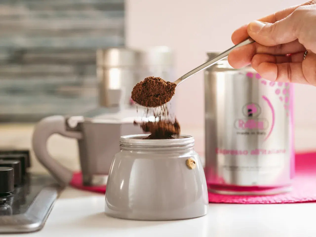 Un cucchiaino di caffè macinato cade nel bricco di una caffettiera, un ricordo di come si faceva il caffè prima della moka.