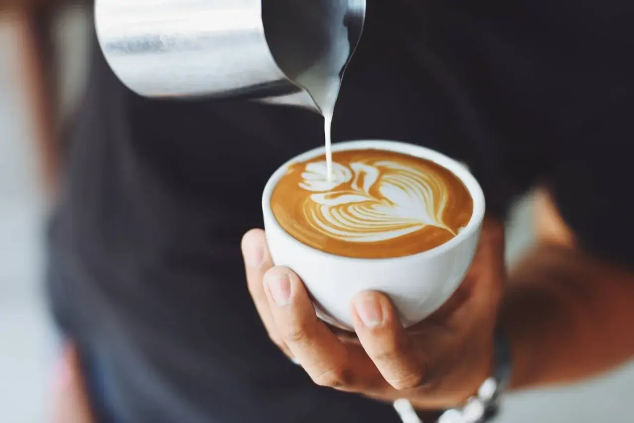 Un barista crea un disegno a latte art su un cappuccino, un'opera d'arte cremosa.