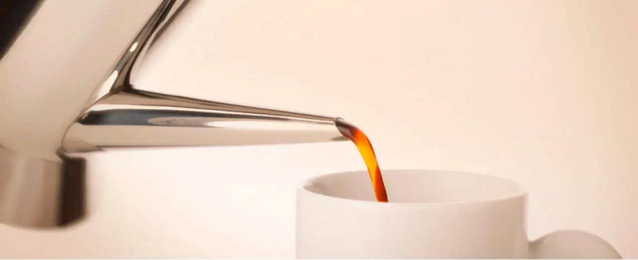 Caffè caldo versato da una cuccuma napoletana in una tazza bianca.