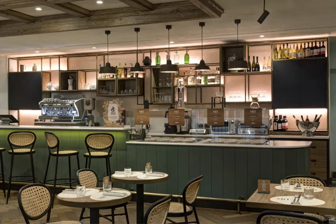 Interno di un locale moderno con bancone, macchine da caffè e tavoli. Un'atmosfera perfetta per gustare un ottimo caffè a Roma, famoso in tutto il mondo.