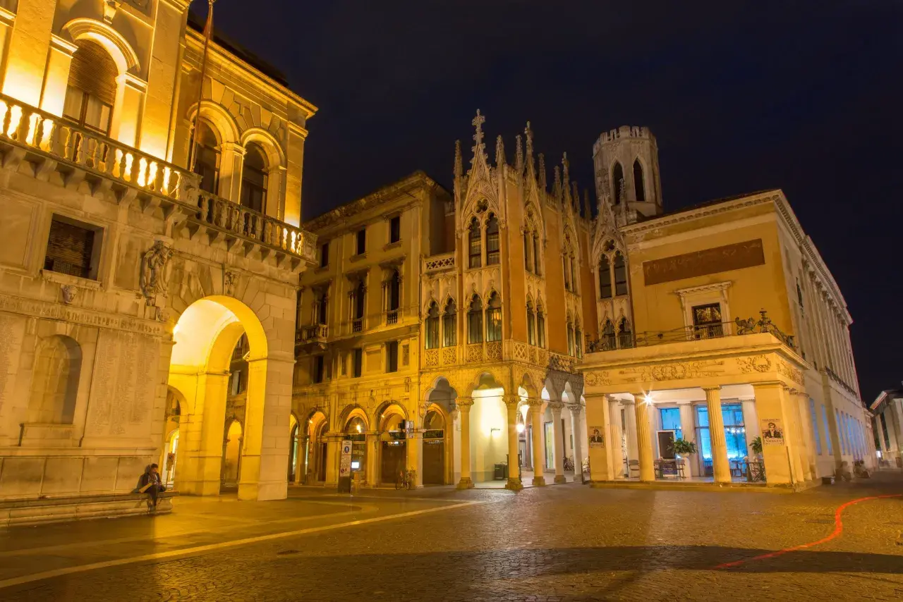 Edificio storico illuminato di notte a Padova, con archi e dettagli gotici. Un luogo che evoca il fascino di un **caffè storico Padova**.
