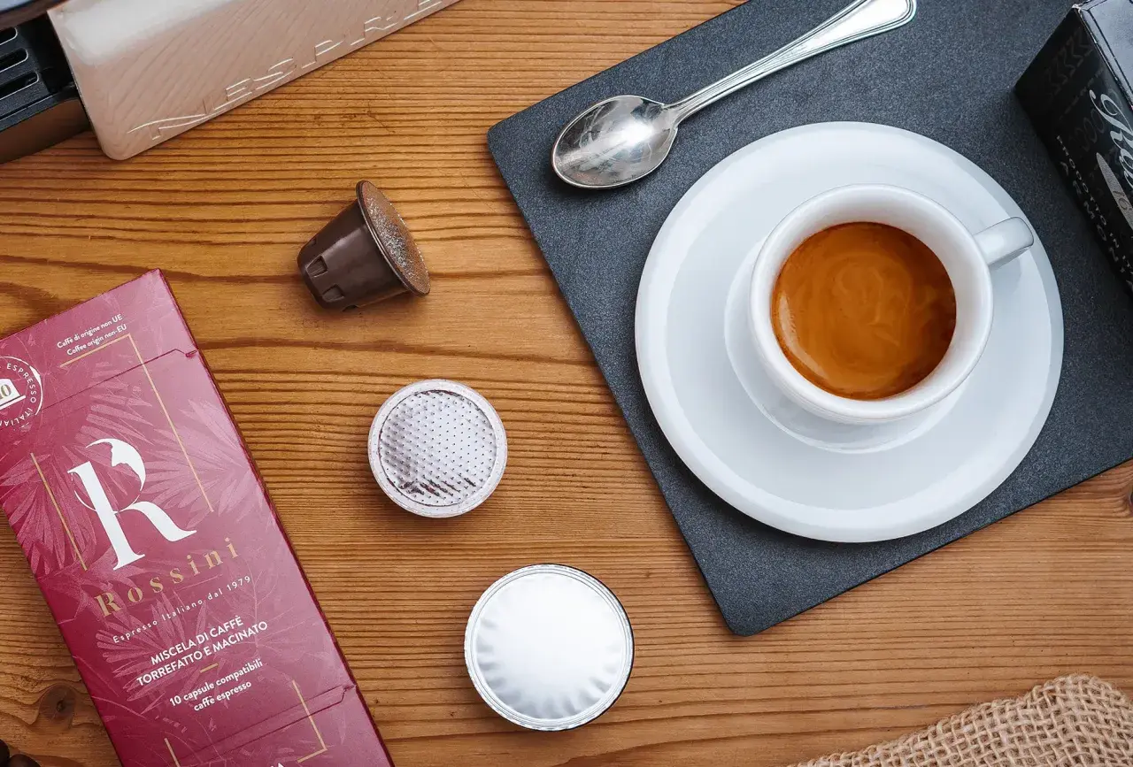 Vari tipi di caffè in capsule, una tazzina di espresso fumante e la confezione Rossini.