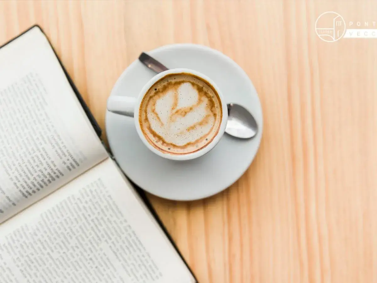 Un libro aperto e una tazza di caffè con schiuma, un invito al caffè illuminismo, su un tavolo di legno.