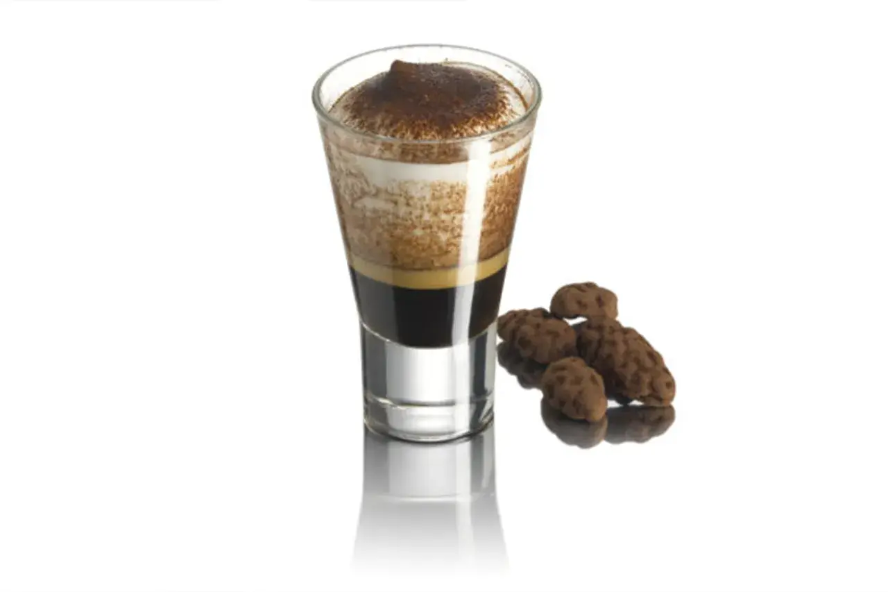 Un bicchierino di caffè con schiuma e cacao, accompagnato da dolcetti al cioccolato.