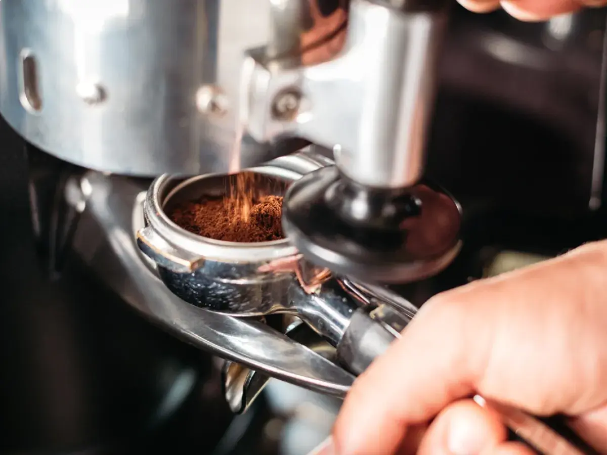 Macinatura caffè bar: polvere scura cade nel portafiltro, pronta per un espresso perfetto.