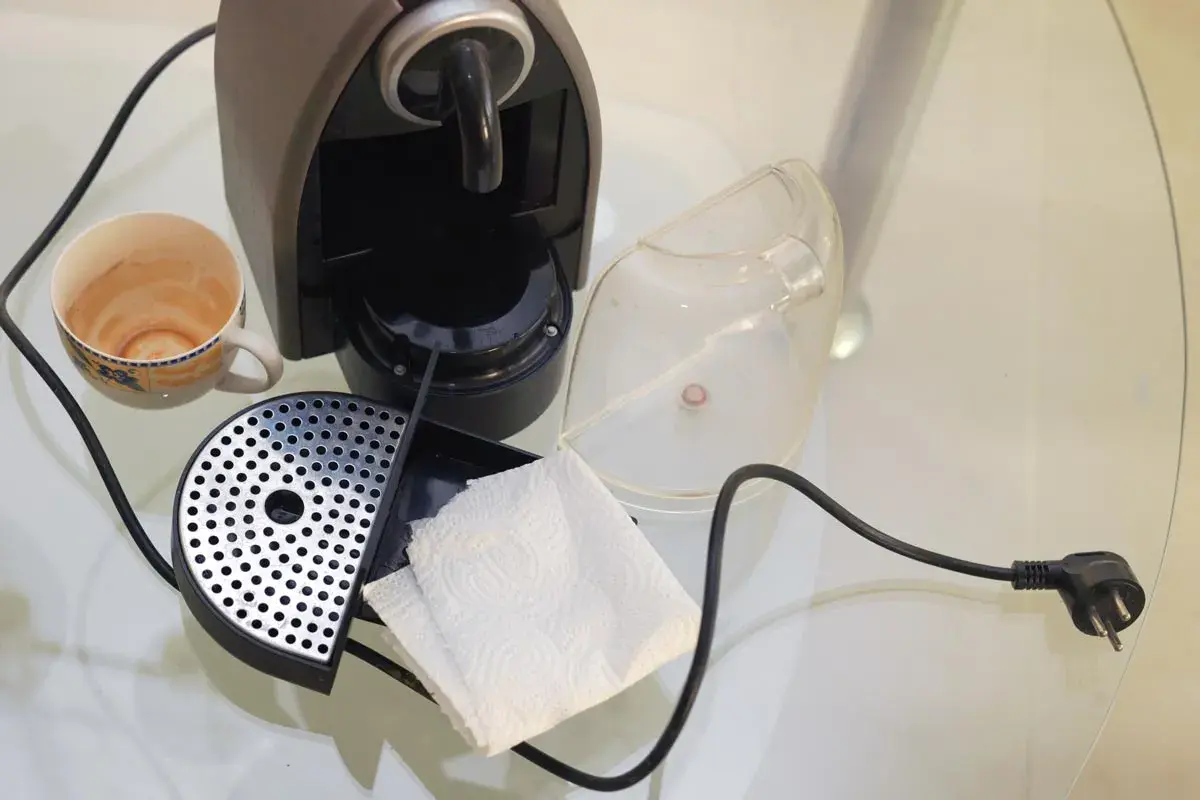 Macchina caffè bar smontata per pulizia: tazzina sporca, vaschetta raccogligocce, serbatoio trasparente e fazzoletti di carta.