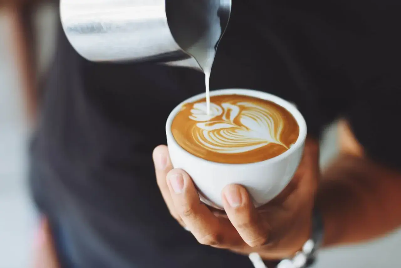 Un barista versa latte montato su un espresso, creando un disegno di latte art. Ecco come si fa il cappuccino perfetto.