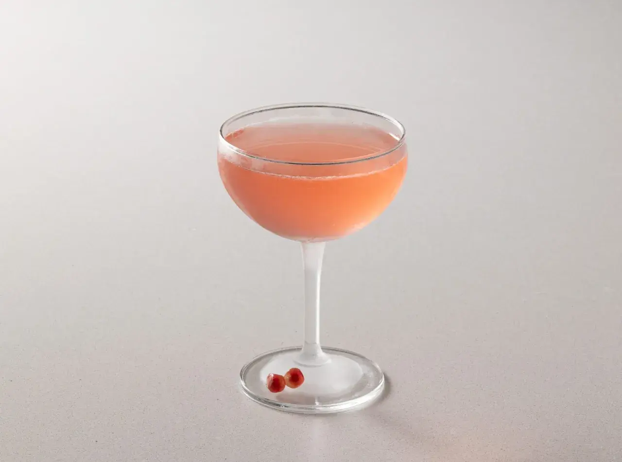 Cocktail rosa in coppa, perfetto per la tua bacardi cocktail ricetta. Due chicchi di melograno sul piattino.