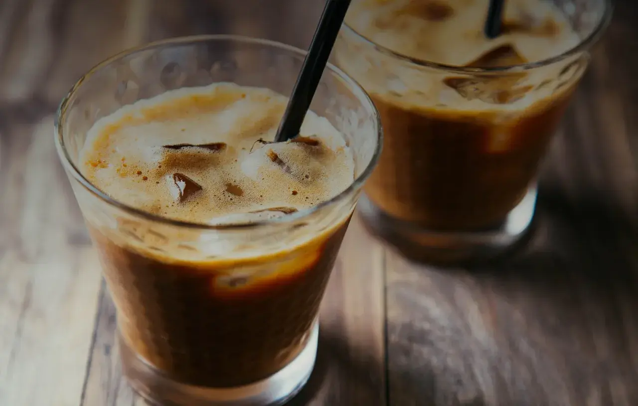 Due bicchieri di **cold brew** con ghiaccio e cannucce nere su un tavolo di legno.