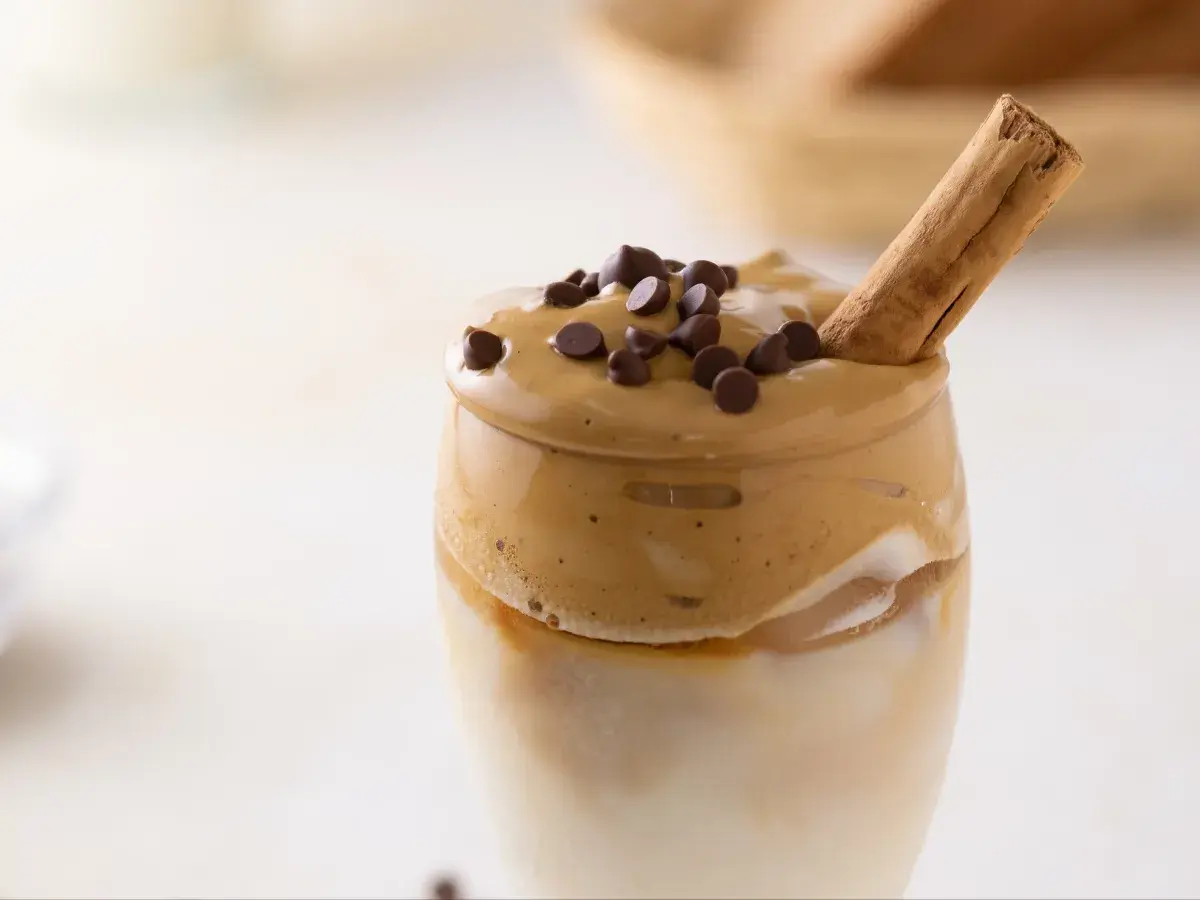Un delizioso caffè freddo, con schiuma cremosa, gocce di cioccolato e un bastoncino di cannella.