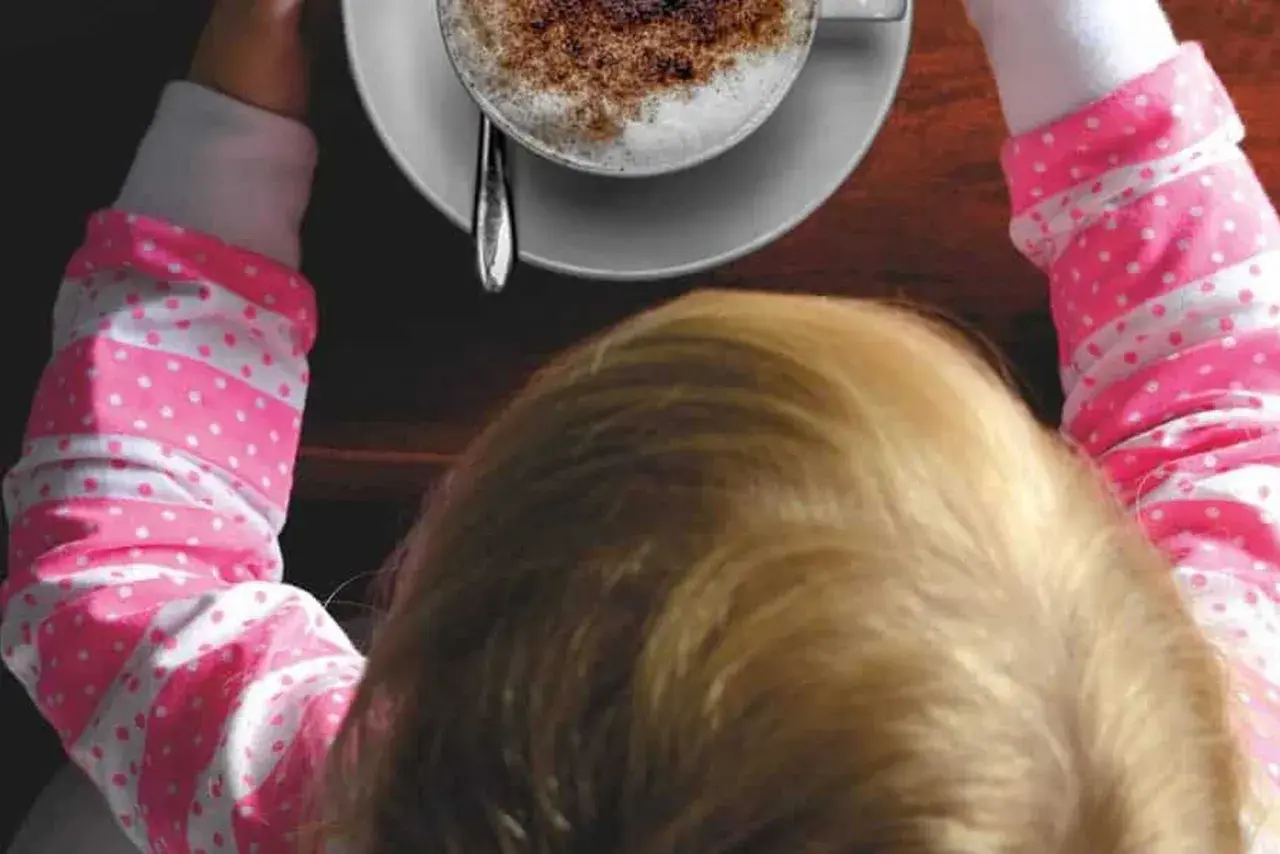 Bambini che gustano un caffè decaffeinato, con una tazza di cappuccino spolverato di cacao.