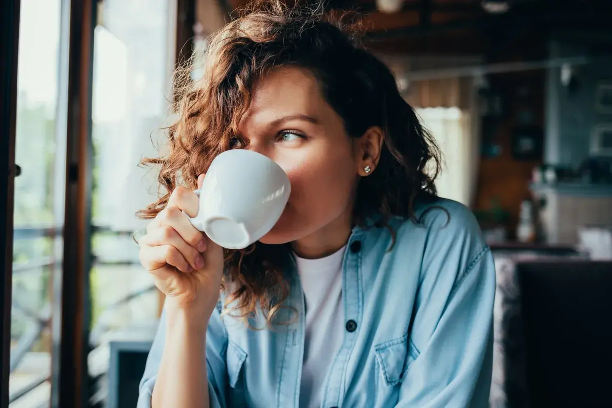 Donna con capelli ricci beve una tazza di caffè, un momento di relax con potassio naturale.