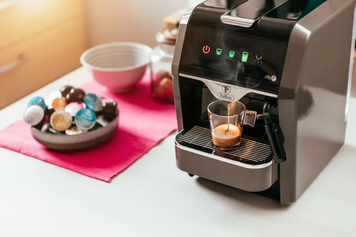 Macchina da caffè prepara un espresso. Accanto, una ciotola piena di capsule colorate, per scegliere se è meglio cialde o capsule.