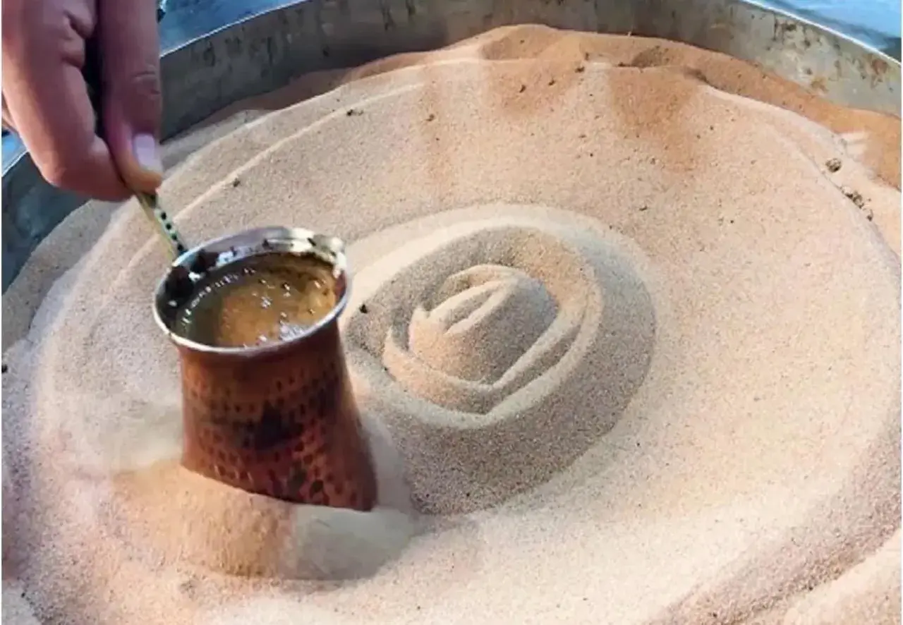 Un cezve di caffè turco viene preparato nella sabbia calda, creando un vortice invitante.