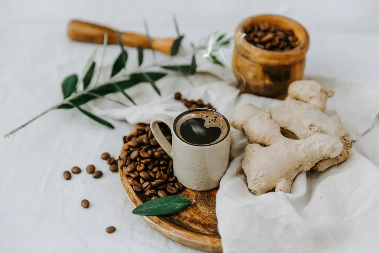 Tazza di caffè messicano fumante, chicchi tostati, zenzero fresco e un rametto d'ulivo su un panno di lino.
