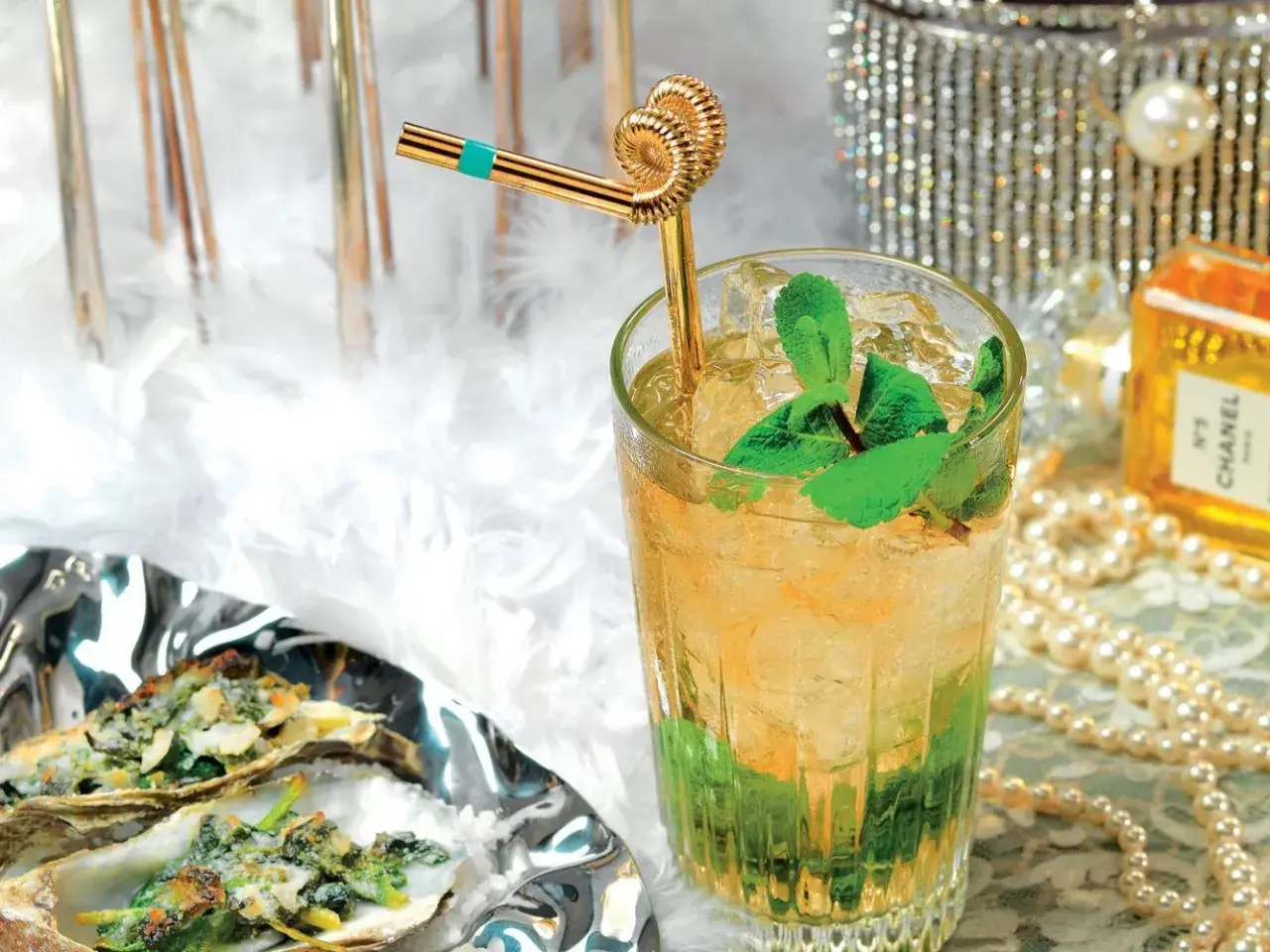 Un rinfrescante cocktail Italia, con menta e ghiaccio, accanto a ostriche gratinate e un flacone di profumo Chanel.